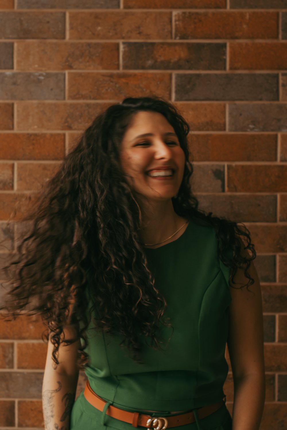 Julia Kalil rindo, encostada numa parede de tijolos